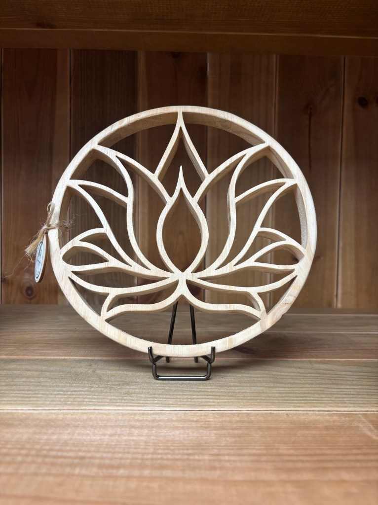 Sculpture en bois représentant une fleur de lotus, exposée sur un support en métal, contre un fond en bois.