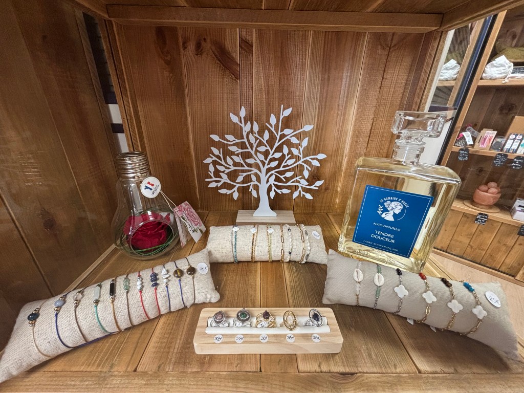 Une étagère en bois contenant des bracelets colorés en pierres naturelles, présentés sur des coussins, un flacon de parfum, et un arbre décoratif en papier.