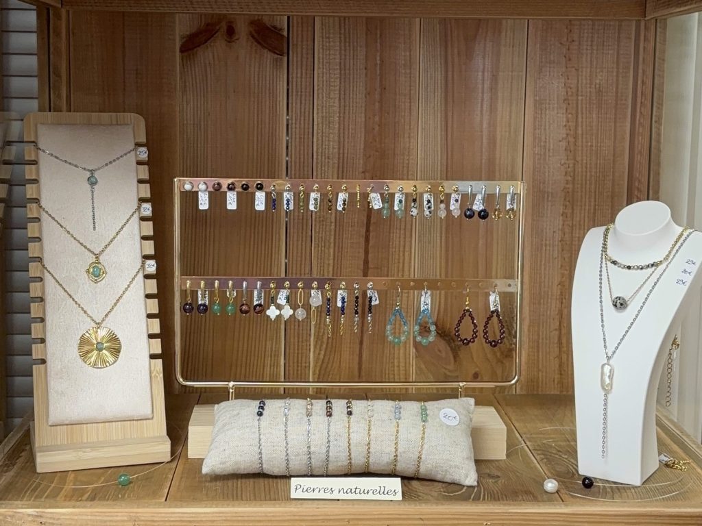 Vitrine avec des bijoux artisanaux en pierres naturelles, comprenant des colliers et des boucles d'oreilles, présentés sur un support en bois.