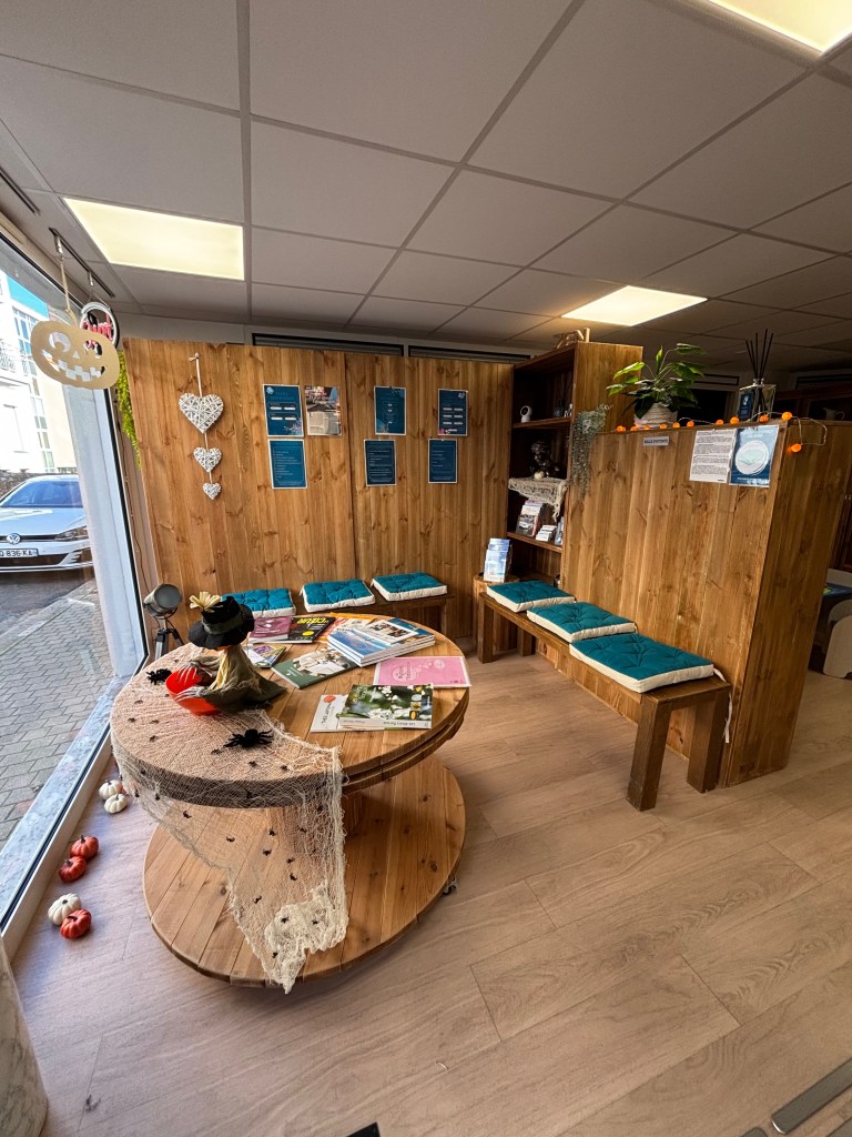 Intérieur d'un espace bien-être avec des murs en bois, des sièges confortables et une table circulaire au centre. Des brochures et magazines sont étalés sur la table. Une décoration chaleureuse avec des plantes et des éléments décoratifs.